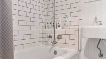 Une salle de bain avec des murs recouverts de carreaux blancs, une baignoire, un lavabo et trois flacons de savon pour les mains Dove sur une étagère.
