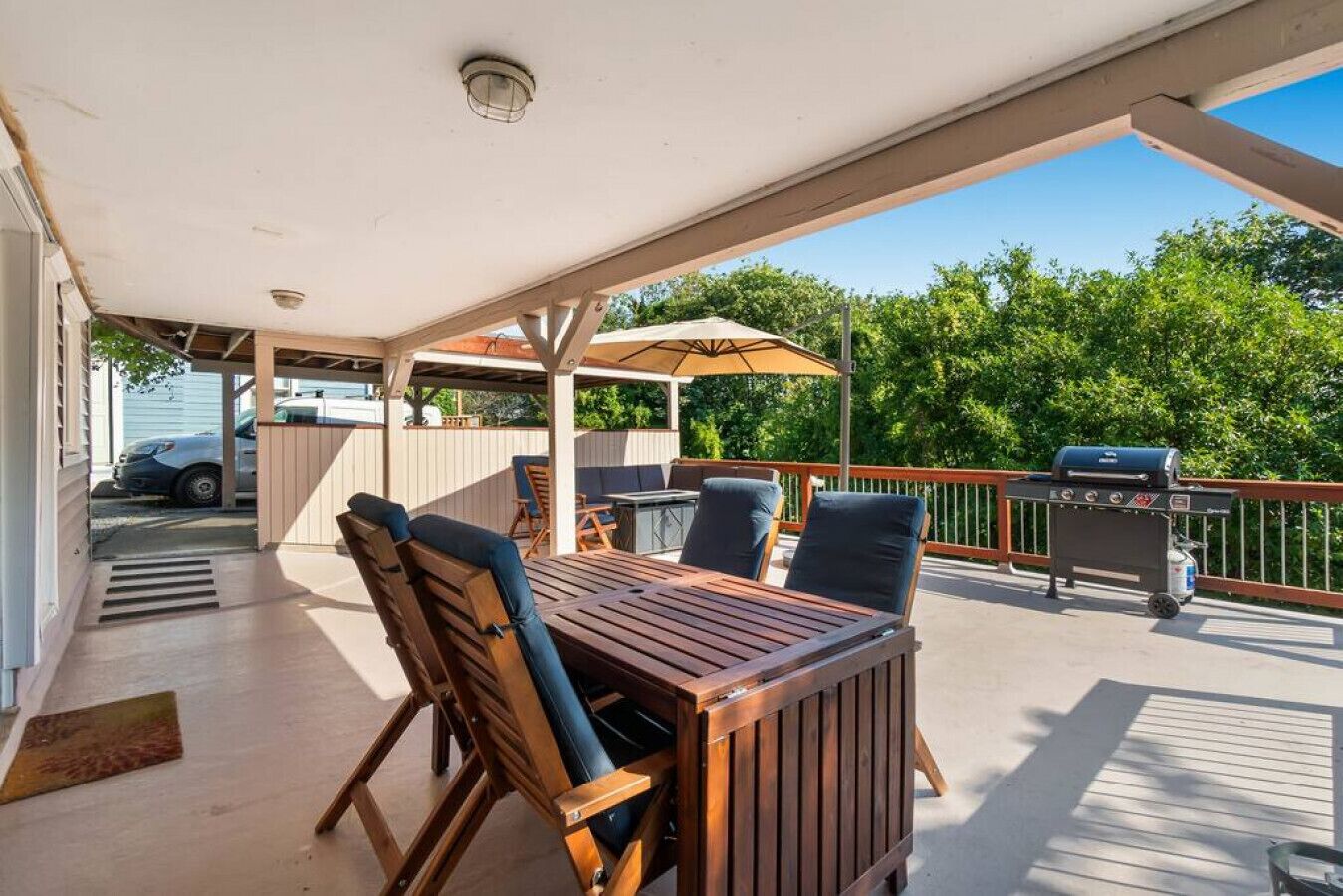 En udendørs terrasse med et træbord og stole, grill og en overdækket siddeplads.