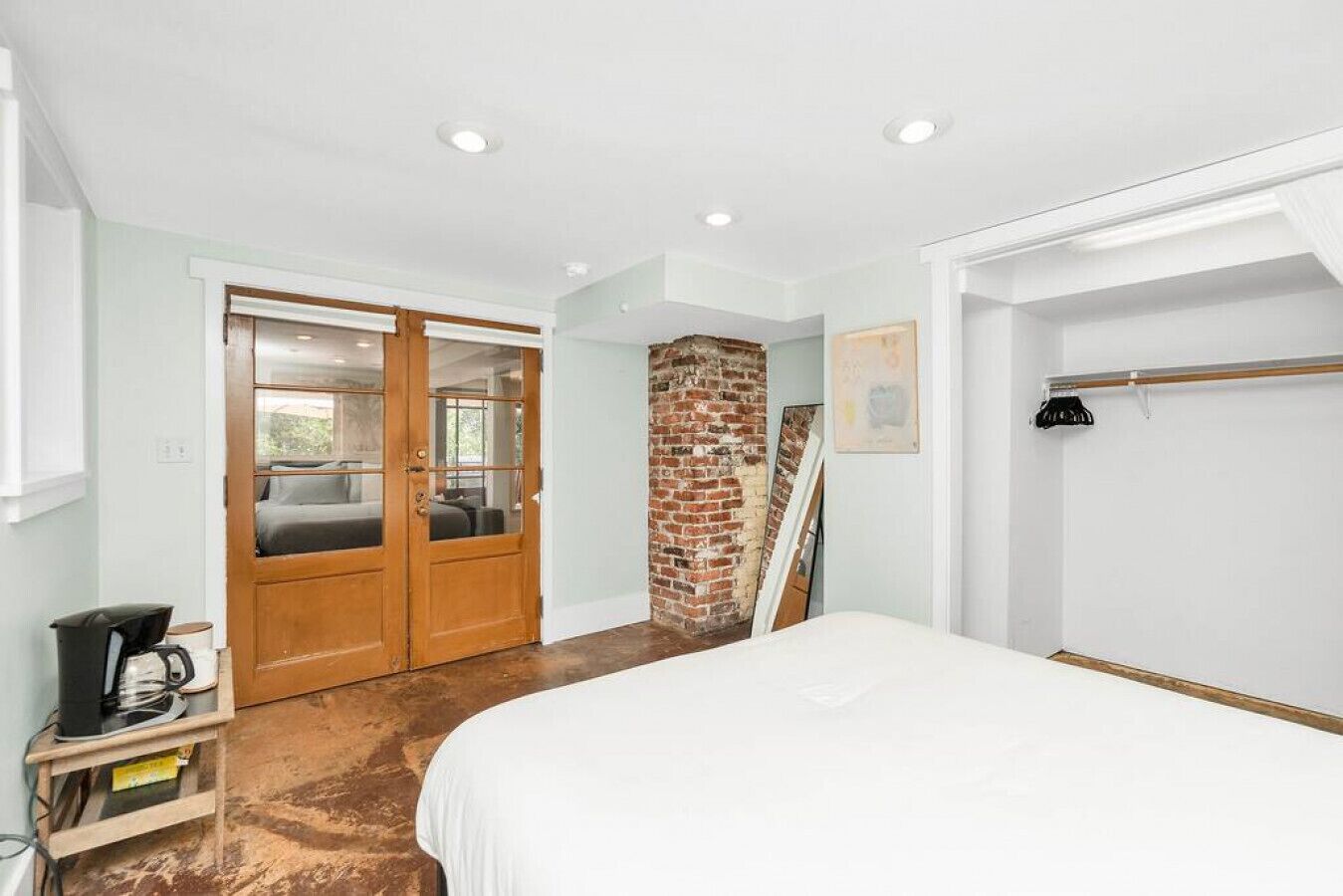 A bedroom with a large bed, a wooden wardrobe, a brick wall, and a ceiling light.