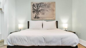 Ein Schlafzimmer mit einem großen Bett, zwei Nachttischen mit Lampen und einem an der Wand hängenden Baumgemälde.