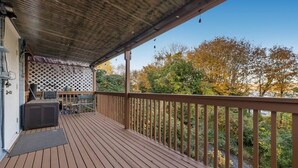 A wooden deck with a covered area, a grill, and a view of trees.
