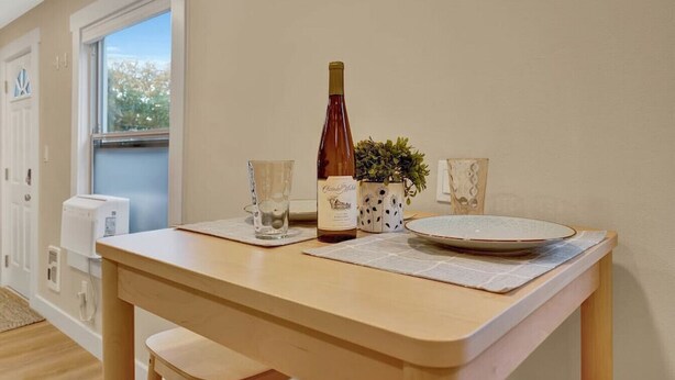 A dining area with a table set for two, a bottle of wine, two glasses, and a small potted plant.