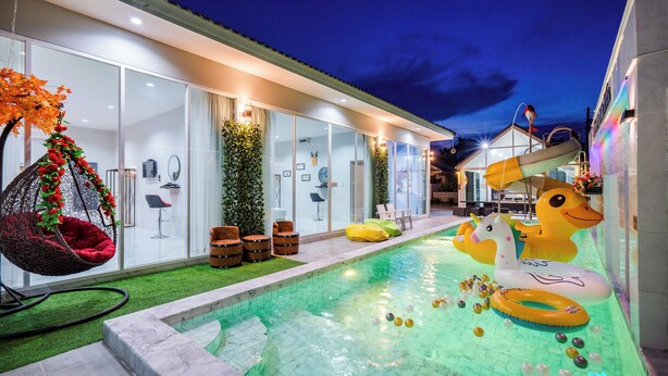 Una casa moderna con piscina, una silla colgante y juguetes inflables.