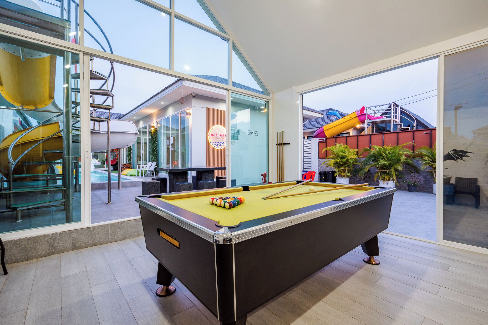 A pool table in a modern indoor space with large windows, a slide, and a pool table in the background.