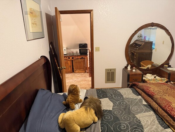 A bedroom with a bed, a dresser, a mirror, and a door leading to a kitchen.
