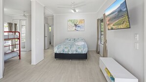 Un dormitorio con cama, literas, ventilador de techo, un cuadro y televisor en la pared.