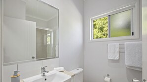 Un baño moderno con un espejo grande, un lavamanos, un inodoro y una ventana con vistas a zonas verdes.
