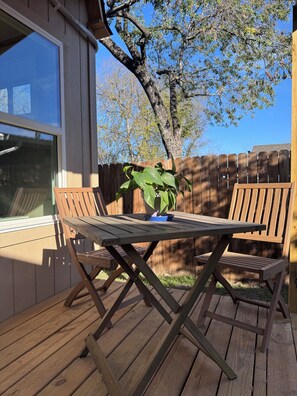 Eine Holzterrasse mit Tisch und zwei Stühlen, einem Blumentopf und einem Holzzaun im Hintergrund.