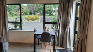 A room with a large window, a dining table with chairs, a sofa, and a TV on the wall.