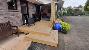 A wooden deck with a bench, a table, and chairs, leading to a building with a brick wall and a mounted animal head.