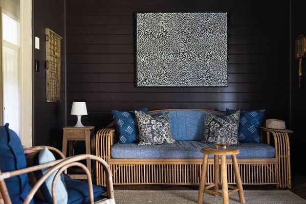 Una pared de madera oscura con un diseño artístico, un sofá de mimbre con cojines estampados, una pequeña mesa de madera y una silla.