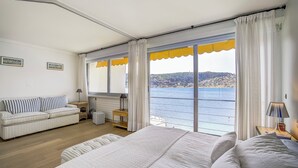 A bedroom with a large bed, a sofa, and a view of the sea.