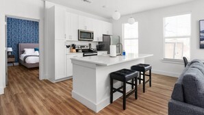 A modern kitchen with white cabinets, a central island with stools, a microwave, and a stove. - Perfect Spot: Cozy Stay & Coffee Shop/Bar Onsite! (Pflugerville)