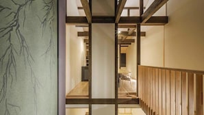 Un intérieur moderne avec un escalier en bois, un coin repas et un mur orné d’un motif rappelant un arbre.