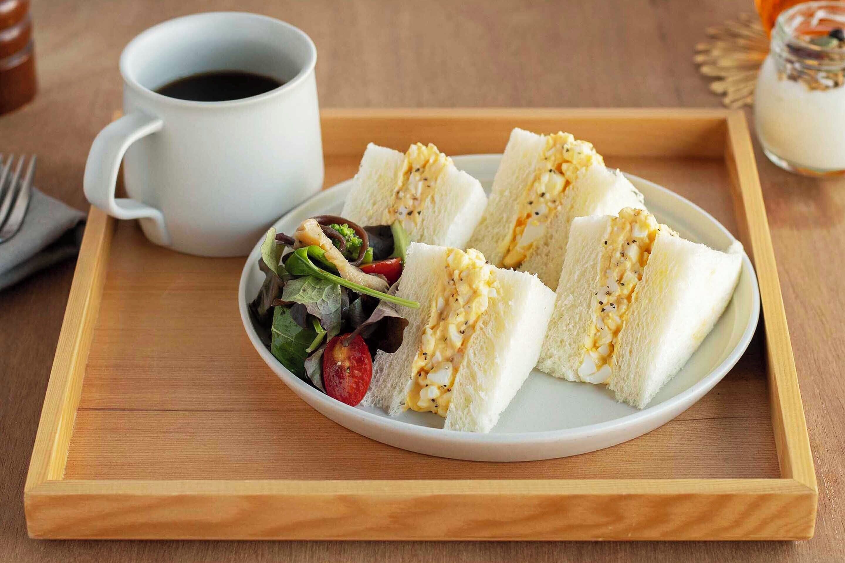 Una bandeja con sándwiches, una taza de café y una ensalada pequeña.