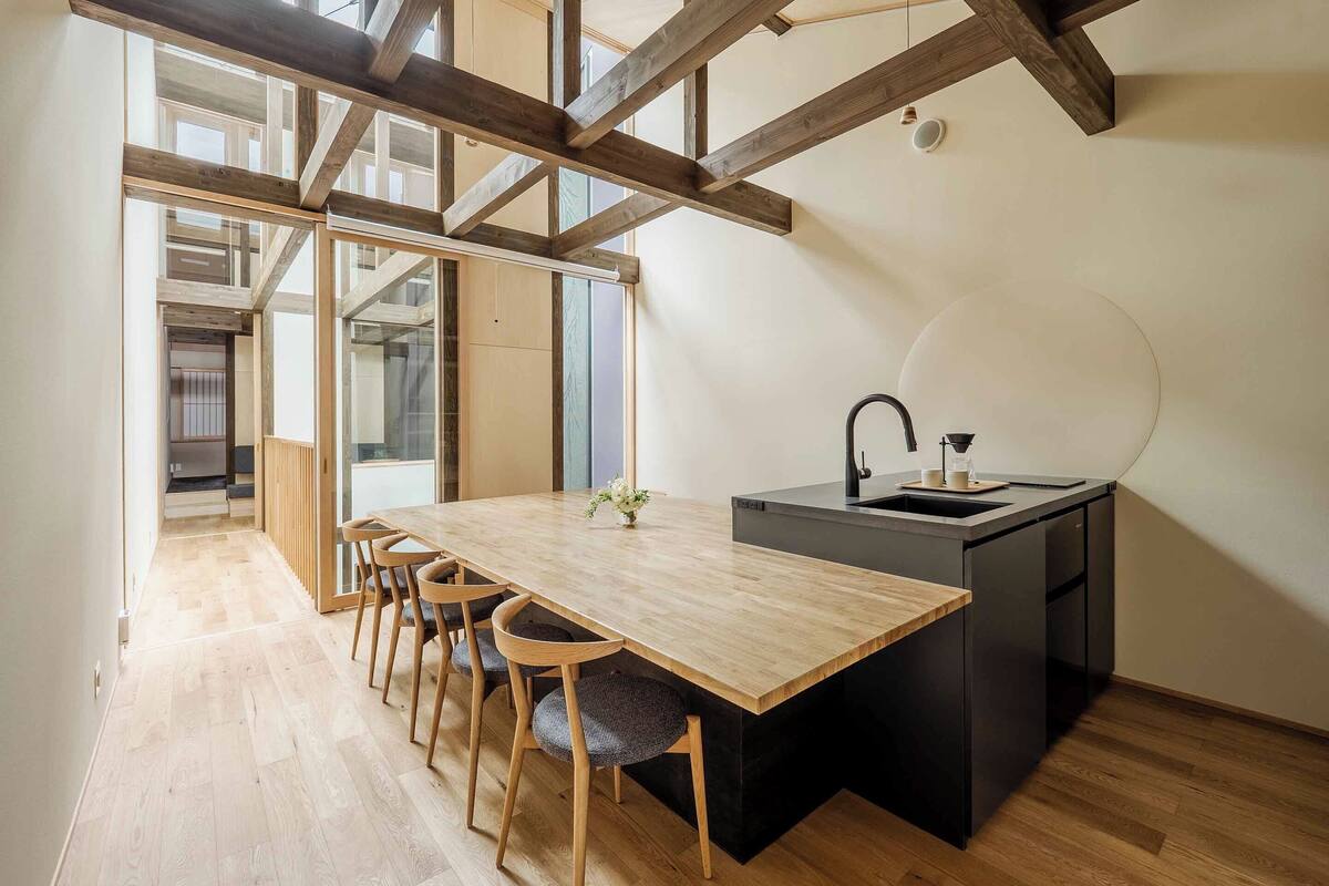 A modern kitchen with a wooden table and chairs, a black sink, and a view of the city.