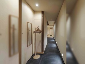Un long couloir étroit, doté d’un plancher sombre, de murs clairs et d’une porte en bois au fond.