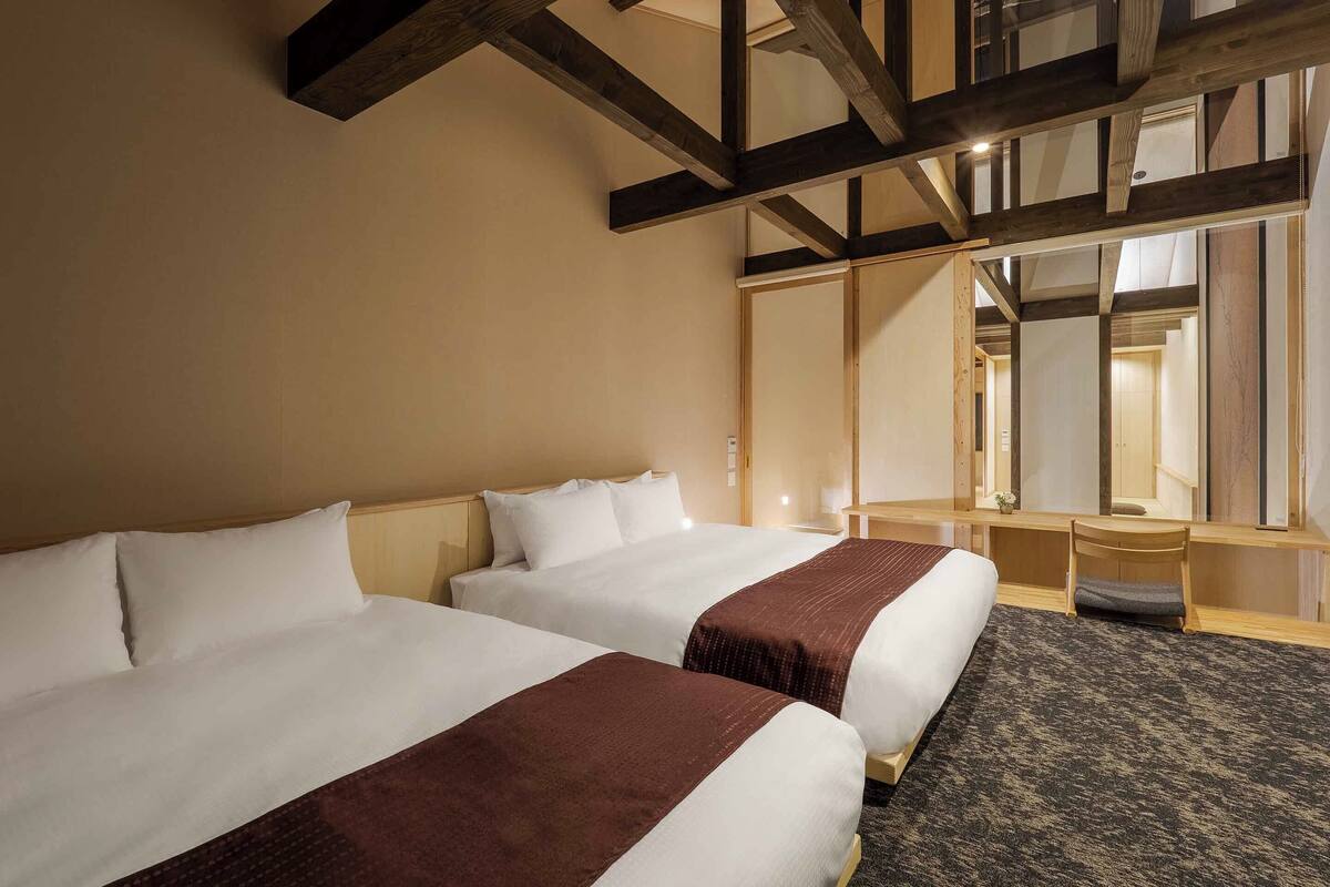 A hotel room with two beds, a desk, and a mirror.