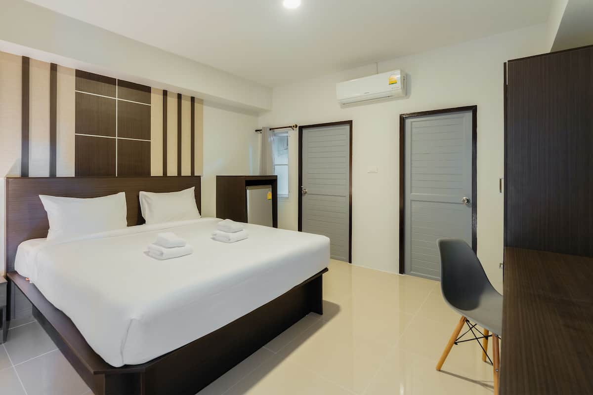 A modern hotel room with a large bed, a bedside table, a desk, and a wardrobe.