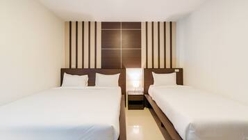 A hotel room with two single beds, a wooden headboard, a nightstand with a lamp, and a wall panel design.