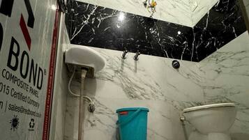 Een badkamer met toilet, bidet en een blauwe emmer op een kruk.