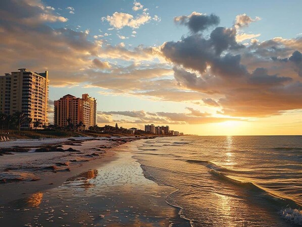Uma praia com edifícios ao fundo durante o pôr do sol.