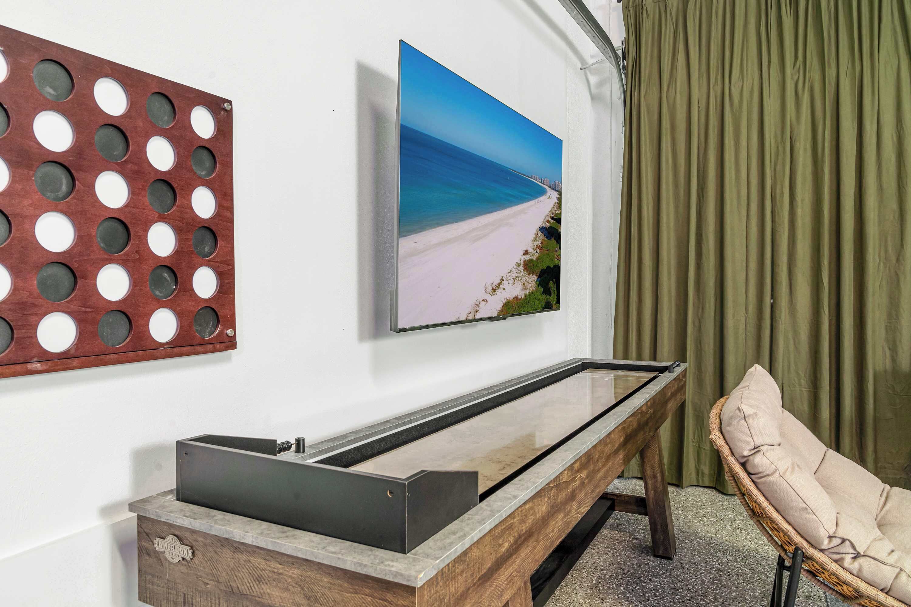 Ein Zimmer mit einem Holztischchen, einem gerahmten Gemälde von einem Strand und einem Korbstuhl.