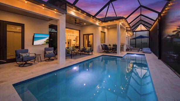 A swimming pool with a glass ceiling, lounge chairs, and a dining area with tables and chairs. - Luxury 5BR - Pool, Game Room, Mini Golf, Fire Pit (Marco Island)
