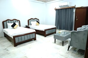 Two single beds with grey headboards and a small ottoman provide comfortable seating in this stylish room.
