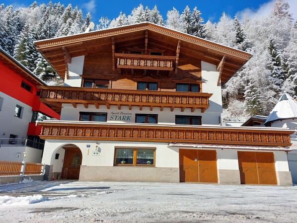 A multi-story building with a wooden balcony, a sign reading "Apart Pension STARK", and a snow-covered landscape.