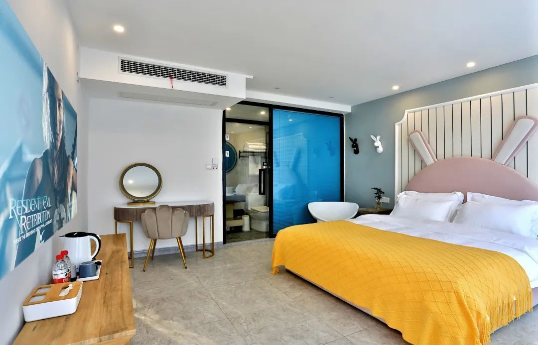 Une chambre d’hôtel moderne dotée d’un grand lit, d’un bureau avec une chaise, d’une petite table avec un miroir et d’une salle de bain visible à travers une porte en verre.