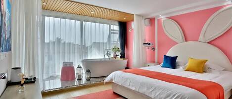 A modern bedroom with a large bed, a bathtub, and a city view.
