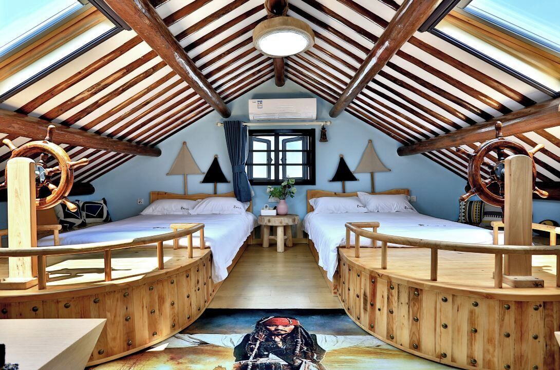 A cozy attic bedroom with two beds, wooden beams, a skylight, and a ship's wheel decoration.