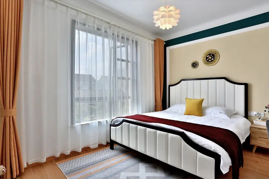 A neatly arranged bedroom with a bed, curtains, a patterned rug, and wall decor.