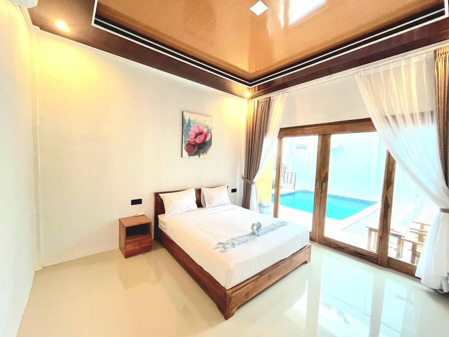 Una habitación de hotel con una cama grande, una mesita de noche, un cuadro y una puerta corrediza de vidrio que da a una zona de piscina.