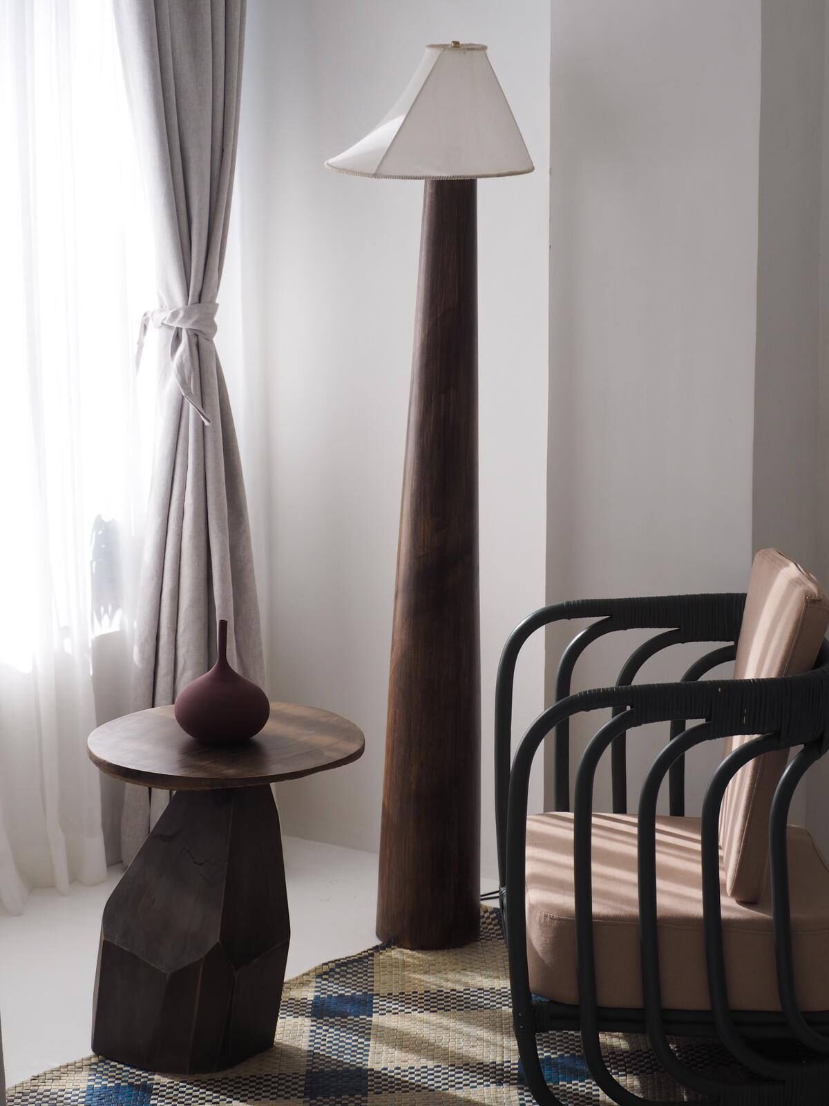 A modern room with a round wooden table, a tall floor lamp, a black metal chair, and a patterned rug.