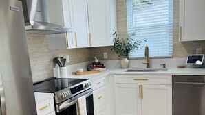 Una cucina moderna con mobili bianchi, elettrodomestici in acciaio inossidabile, forno integrato e una finestra con persiane.