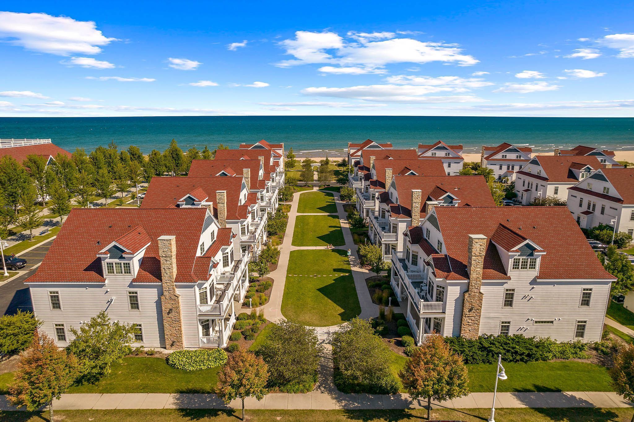 A residential area with multiple two-story houses, a central lawn, and a view of the ocean.