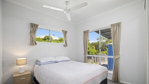 A bedroom with a bed, a bedside table with a lamp, a ceiling fan, and a window with curtains. - HONU, part of the Ohana Surf Bungalows (<5 minute walk to beach and shops). (Scotts Head)