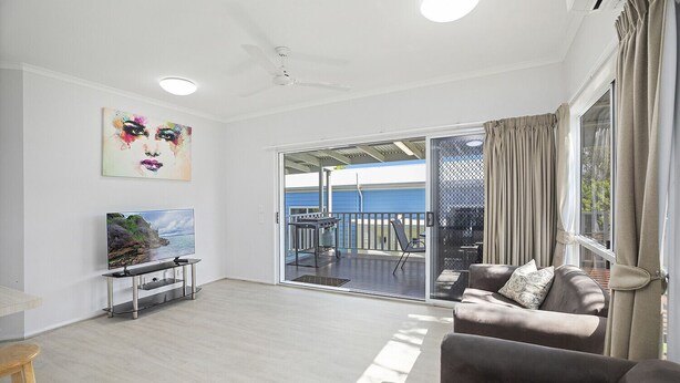 A spacious living room with a flat-screen TV, a sofa, and a sliding glass door leading to an outdoor patio. - HONU, part of the Ohana Surf Bungalows (<5 minute walk to beach and shops). (Scotts Head)