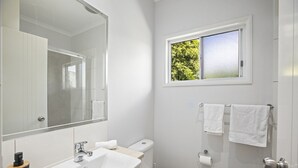 A bathroom with a white sink, toilet, and a window with a view of greenery. - HONU, part of the Ohana Surf Bungalows (<5 minute walk to beach and shops). (Scotts Head)