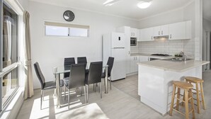 A modern kitchen with white cabinets, a central island, and a dining area with a glass table and chairs. - HONU, part of the Ohana Surf Bungalows (<5 minute walk to beach and shops). (Scotts Head)