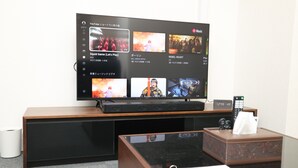 Habitación de hotel con televisor de pantalla plana mostrando un video musical, un escritorio con control remoto y una caja de pañuelos.