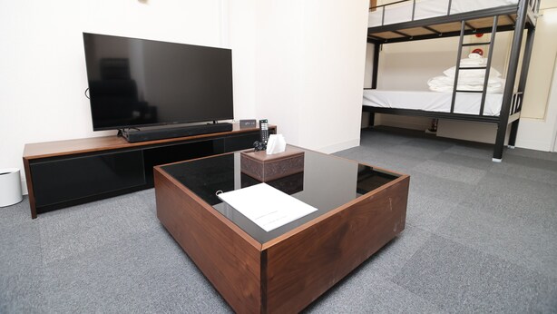 Una habitación moderna con televisor de pantalla plana, una mesa de centro de madera, una cama litera y suelo alfombrado.
