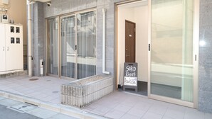 Un edificio moderno con un amplio cerramiento de vidrio corredera, un cartel anunciando Soko Resort Asakusa y un pequeño espacio de asientos al aire libre.