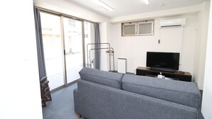 Una sala de estar moderna con un sofá gris, un televisor de pantalla plana y un ventanal corredero que da a un espacio exterior.