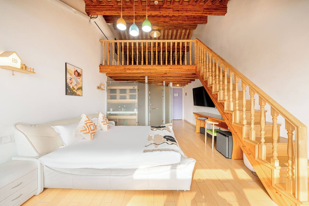A bedroom with a large bed, a wooden staircase, and a balcony.