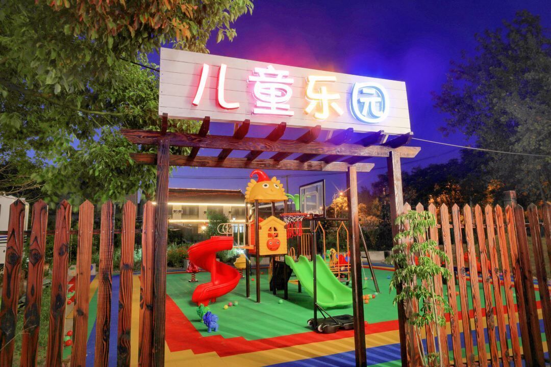 Zona de juegos infantiles con valla de madera, tobogán y estructura para escalar.