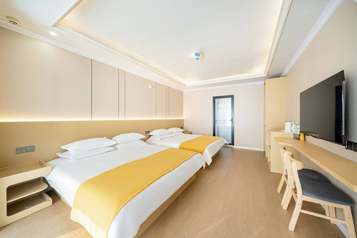 A modern hotel room with two beds, a desk, and a TV.