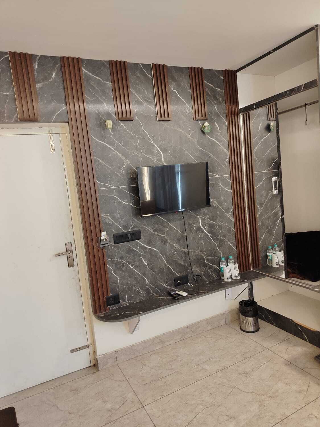 A modern bathroom with a marble backsplash, a mounted TV, a vanity with a mirror, and a door.